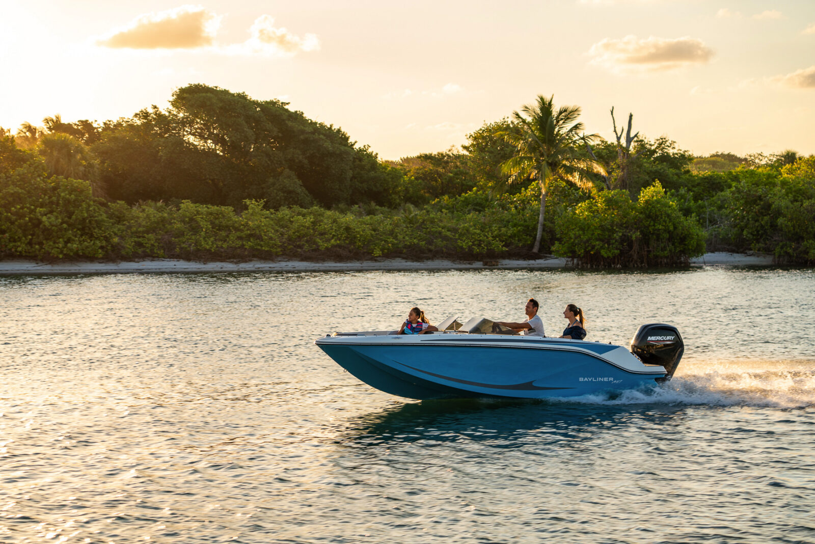 Barco Bayliner con motor Mercury surcando la costa, familias en lancha en la puesta de sol