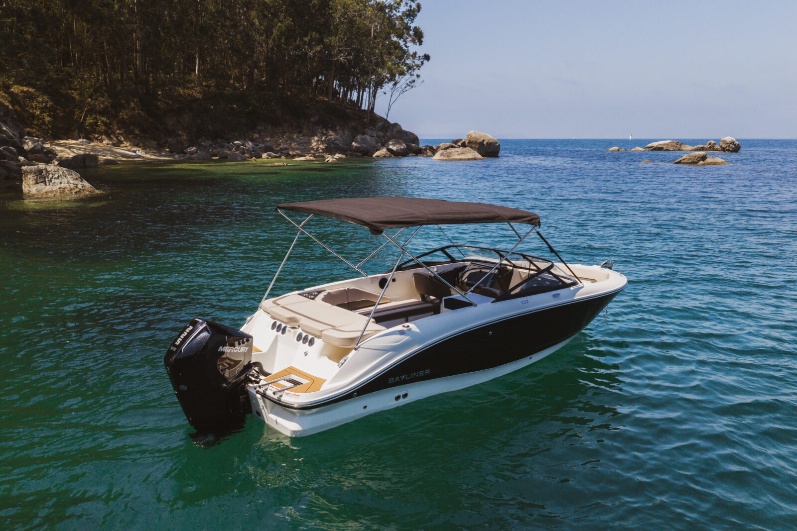 Lancha motora Bayliner blanca con motor Mercury fondeada en una caleta junto al mar