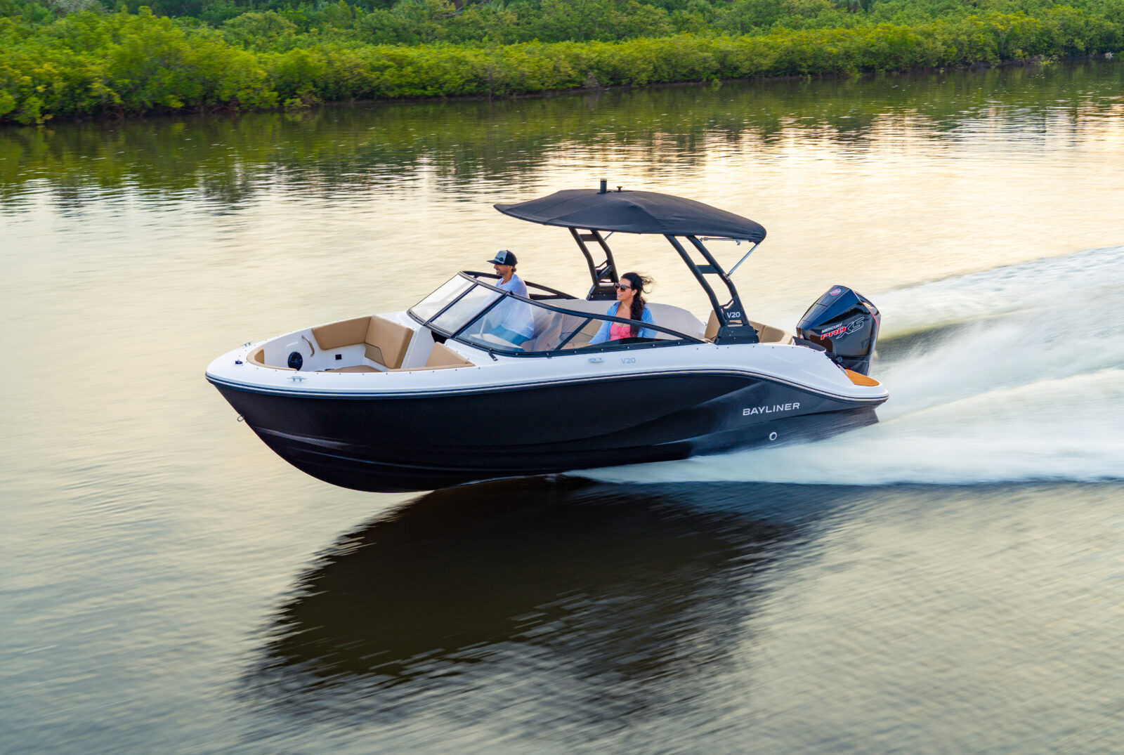 Bote Bayliner V20 en el agua con dos personas, navegación en un lago rodeado de vegetación