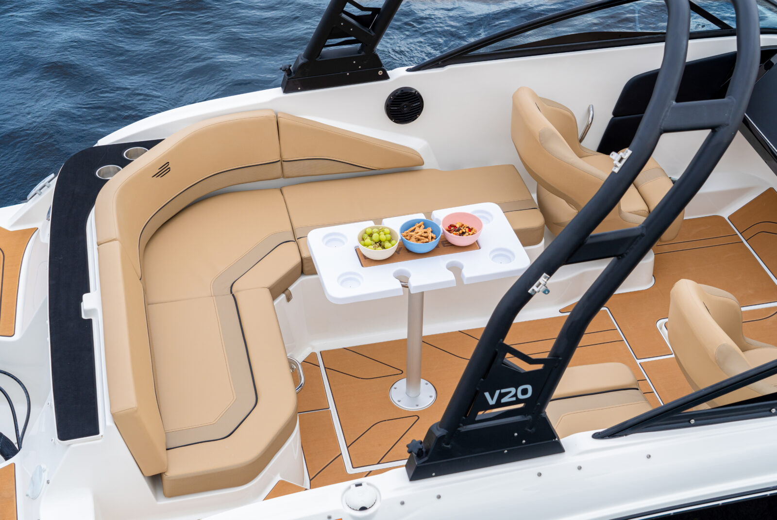 Interior de yate Bayliner V22 con asientos beige y mesa de picnic con snacks a bordo, junto al mar